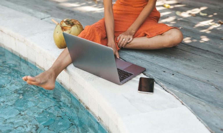 A woman sitting by a pool with a laptop computer